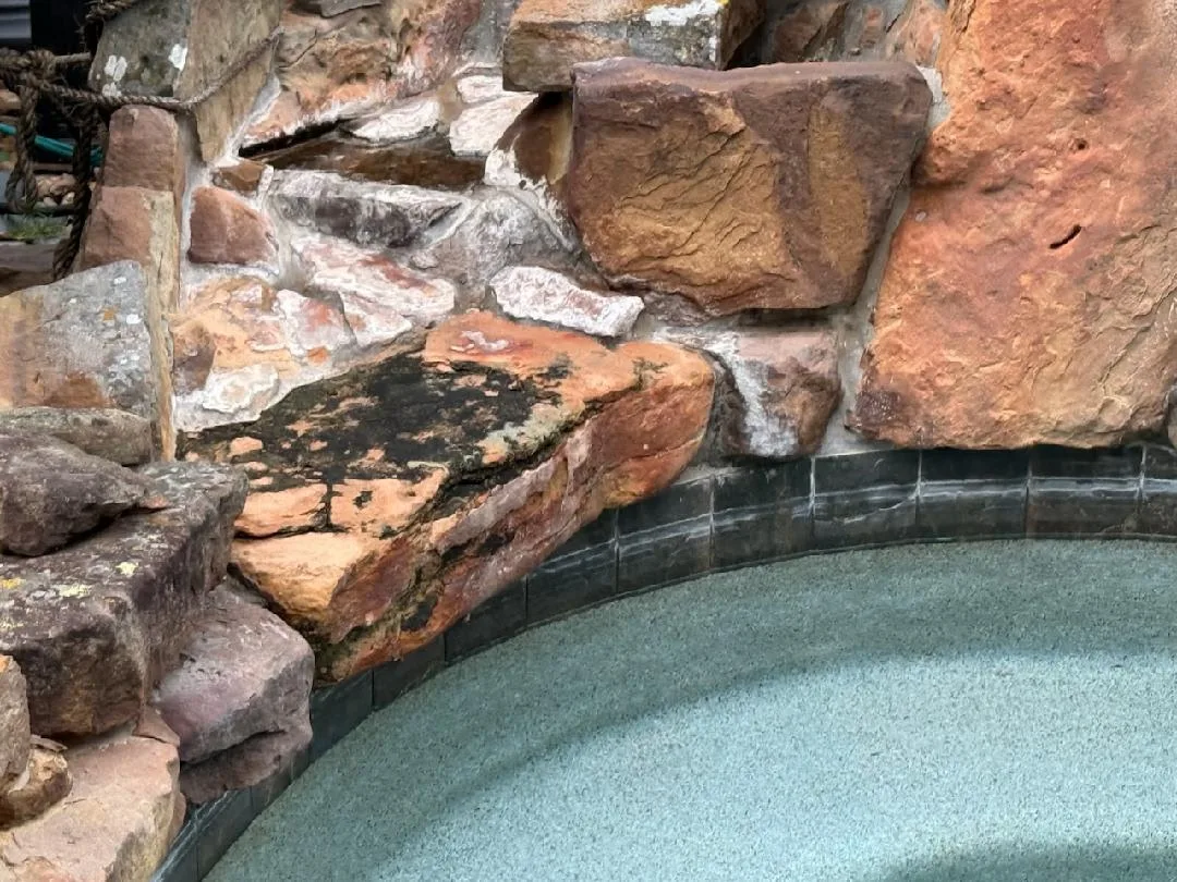 Pool rock waterfall covered in white calcium scale and dark algae staining before bead blasting in Cypress TX